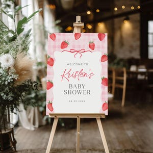 May include: Welcome to Kristen's Baby Shower sign with a pink and white gingham background and red strawberries. The date is 08.20.20XX.