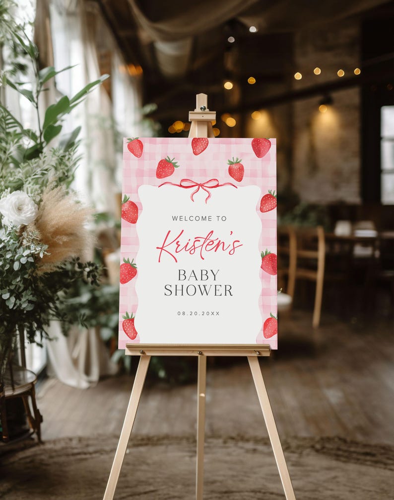May include: Welcome to Kristen's Baby Shower sign with a pink and white gingham background and red strawberries. The date is 08.20.20XX.