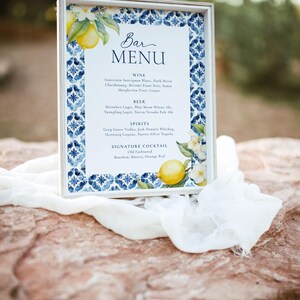 May include: A white framed sign with a blue and white tiled pattern border. The sign has a handwritten title "Bar Menu" and lists various wine, beer, spirits, and a signature cocktail.