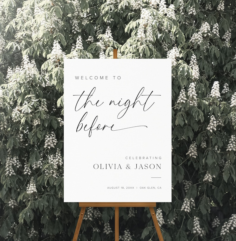 K&ouml;nnte beinhalten: Ein wei&szlig;es Schild mit schwarzem Text, auf dem steht "Willkommen zur Nacht vor der Feier von Olivia & Jason am 18. August 20XX in Oak Glen, CA". Das Schild steht auf einem Staffelei vor einem gr&uuml;nen Busch mit wei&szlig;en Bl&uuml;ten.