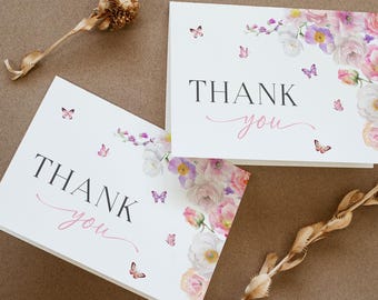 May include: Two white thank you cards with pink and purple watercolor floral designs and butterflies. The text "Thank you" is written in pink cursive on both cards.