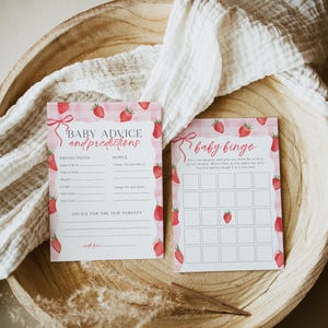 May include: Two pink and white cards with a strawberry theme. The first card has the text "Baby Advice and Predictions" and has spaces to write in predictions and hopes for the baby. The second card has the text "Baby Bingo" and has a bingo card with strawberry images.