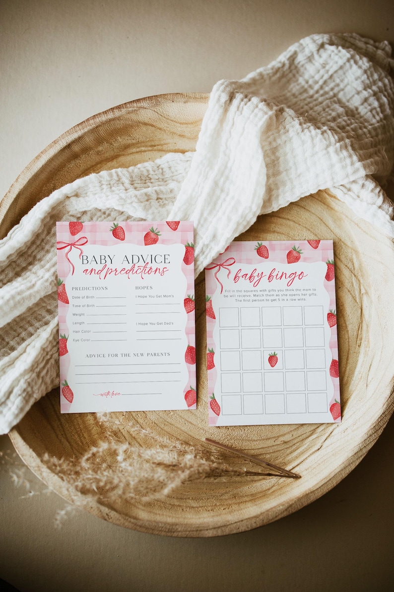 May include: Two pink and white cards with a strawberry theme. The first card has the text "Baby Advice and Predictions" and has spaces to write in predictions and hopes for the baby. The second card has the text "Baby Bingo" and has a bingo card with strawberry images.