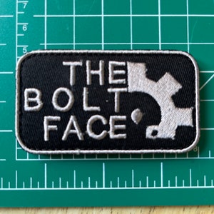 May include: A black and white embroidered patch with the text "THE BOLT FACE" and a stylised mountain range design.