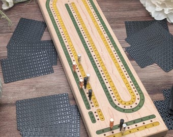 May include: A wooden cribbage board with green and yellow inlaid tracks, and metal pegs. The board is rectangular with rounded ends. Several decks of gray playing cards with a dotted pattern are scattered around the board.