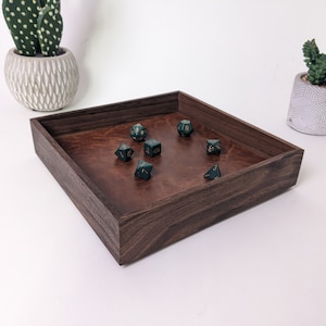 May include: A dark wood tray with a brown felt lining. The tray is filled with green dice with gold numbers.