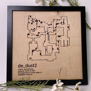 May include: A framed wooden map of the popular Counter-Strike: Global Offensive map de_dust2. The map is laser-cut into the wood and features the text "de_dust2", "creator: david johnson", "released: march 13, 2001", "first appearance: counter strike 1.1", and "Inspiration: morocco".