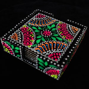 Puede incluir: Un juego de seis posavasos negros con un diseño floral colorido. Los posavasos están apilados y tienen un borde blanco con puntos negros.