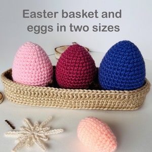 May include: A woven basket holds three crocheted Easter eggs in pink, burgundy, and blue. The basket is made of a light brown material. The text "Easter basket and eggs in two sizes" is at the top of the image. A single peach-colored egg is in the foreground.