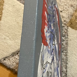 K&ouml;nnte beinhalten: Ein graues Leinwandbild mit einem roten, wei&szlig;en und blauen abstrakten Design. Das Bild ist auf einer dreieckigen Leinwand.