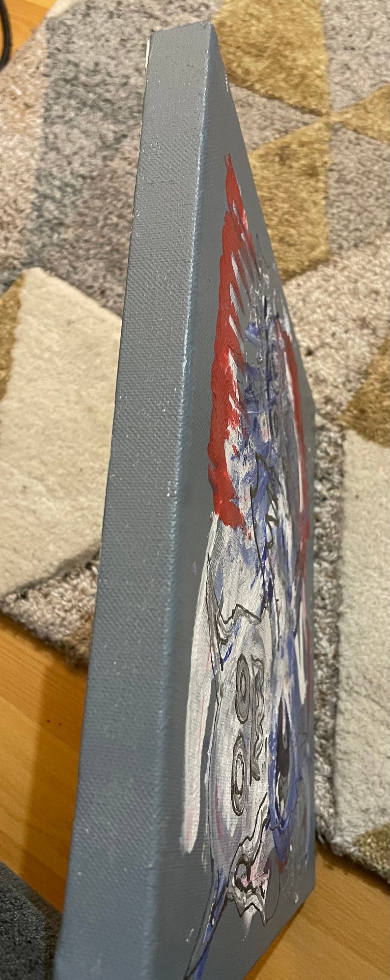 K&ouml;nnte beinhalten: Ein graues Leinwandbild mit einem roten, wei&szlig;en und blauen abstrakten Design. Das Bild ist auf einer dreieckigen Leinwand.