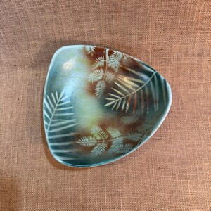 May include: A triangular ceramic bowl with a teal and brown color scheme. The bowl features a fern leaf design in white. The bowl is a decorative piece, suitable for serving snacks or as a display item.