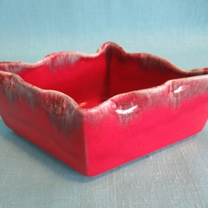 May include: A square ceramic planter with a red glaze and a white glaze on the edges. The planter has a wavy rim.