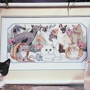 May include: Cross stitch pattern featuring a framed image of a group of cats in a garden setting. The pattern is titled "Purrfect Garden" and is by Eileen Hayes. The pattern is from Dimensions.