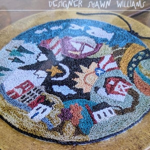 May include: A punch needle embroidery kit featuring a colourful, circular design with various symbols and images. The kit is titled "Threads That Bind" and "My World" and is designed by Shawn Williams. The kit is for a 15.2 cm round punch needle embroidery project.