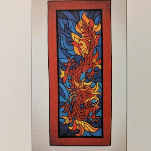 May include: A rectangular stained glass appliqué pattern titled THE DRAGON TSS 2000. The design features a red and yellow dragon with a long tail against a blue background, enclosed in a red border. Text reads: Designs for a life made by hand.