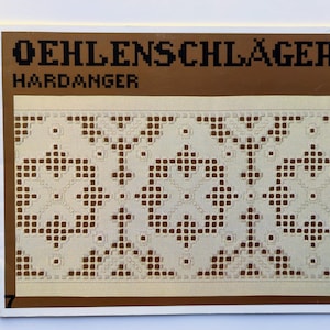May include: A rectangular piece of off-white fabric with a detailed, geometric pattern in brown. The fabric is set against a brown background with the text "OEHLENSCHLÄGER HARDANGER" in black, and the number "7" in the lower left corner.
