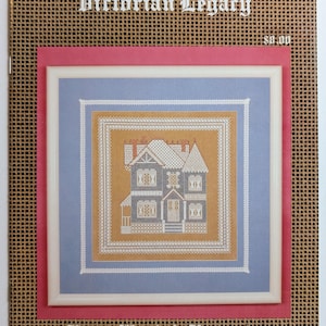 May include: A pattern booklet titled Victorian Legacy and Fancy Work & Fantasies featuring a cross-stitch design of a dark blue Victorian house with white trim on a gold background, framed in a white border against a light blue and pink mat.