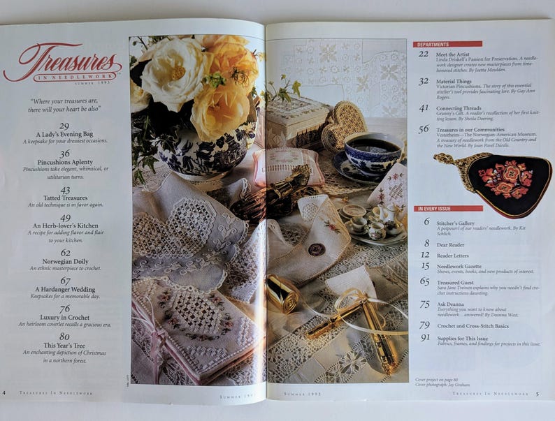 Op de afbeelding: Een tijdschriftpagina met een bloemstilleven, een kopje thee en borduurwerk. Het tijdschrift heet "Treasures in Needlework". De afbeelding bevat een lijst met artikelen en rubrieken.