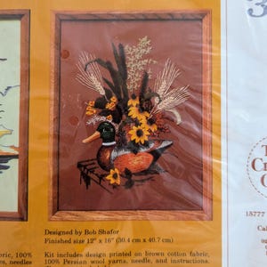 May include: An embroidery kit package titled 0330 Wooden Decoy, featuring a mallard duck and floral arrangement design on brown fabric. The package text specifies a finished size of 12 inches by 16 inches and includes wool yarns and a needle.