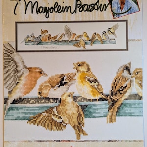 May include: A cross-stitch pattern showing a detailed illustration of birds on a wooden structure. The design includes the text "The Pecking Order" and "Mayjolein Bastin". The Lanarte Leisure Arts logo is visible at the bottom.