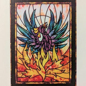 Puede incluir: Una impresión artística rectangular con una ilustración estilo vidriera de un fénix surgiendo de las llamas. El ave tiene plumas moradas, azules y amarillas, mientras que el fuego es naranja, rojo y amarillo. El texto inferior dice PHOENIX TSS 2011.