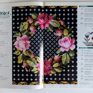 Op de afbeelding: Een tijdschriftpagina met kruissteekpatronen. De omslag toont een zwarte achtergrond met een bloemenontwerp van roze rozen en groene bladeren. De titel van het tijdschrift is "Treasures in Needlework".