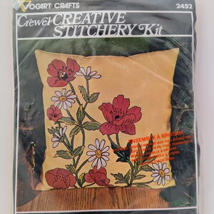 May include: A Vogart Crafts Crewel Creative Stitchery Kit. The kit features a pillow cover with a floral design of red poppies and white daisies on a yellow background. The pillow measures 33 cm x 33 cm when finished. Packaged in a clear plastic bag.