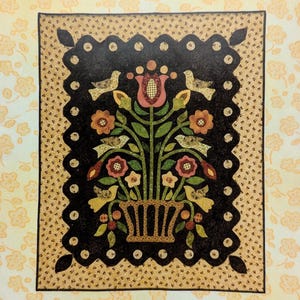 Op de afbeelding: Een ansichtkaartontwerp getiteld "Postcard from the Past" met een bloemstuk in een mand met vogels. Het ontwerp heeft een zwarte achtergrond met een geschulpte rand. Het logo van The Rabbit Factory staat onderaan.