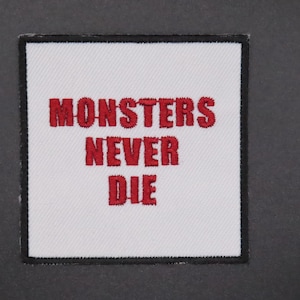Peut inclure: Écusson carré blanc avec bordure noire, brodé du texte rouge "MONSTERS NEVER DIE". Ce patch est conçu pour être cousu ou repassé sur des vêtements ou accessoires.