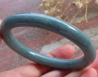 May include: A jade bangle bracelet in a light blue-green colour. The bangle is smooth and polished, with a glossy finish.