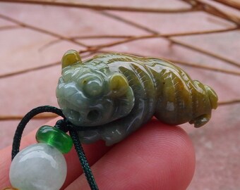 May include: A green and yellow jade pendant carved in the shape of a mythical creature. The pendant is attached to a green cord with a white jade bead.