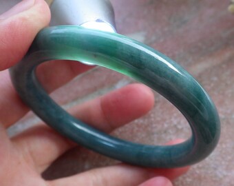 May include: A green jade bangle bracelet. The bangle is smooth and polished, with a slight variation in the shade of green.