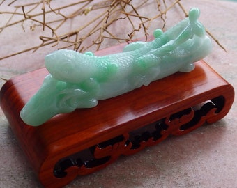 Puede incluir: Una talla de jade de un dragón con un esquema de color verde y blanco. El dragón está descansando sobre un soporte de madera con intrincados tallados.
