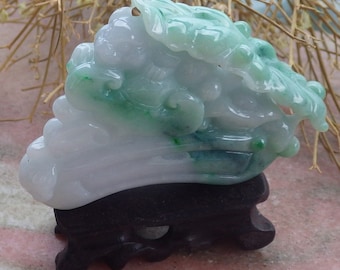 Puede incluir: Una talla de jade de una col con coloración verde y blanca. La col está sentada sobre un soporte de madera negro.