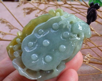 May include: A jade pendant carved in a light green and yellow color. The pendant has a detailed design with a series of raised circular elements. It is suspended from a dark brown cord with green and black beads.