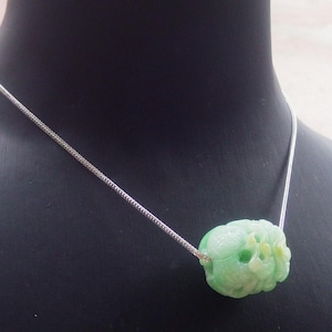May include: A light green jade pendant necklace. The pendant is carved with floral details and hangs from a delicate silver chain. The necklace is displayed on a black mannequin.