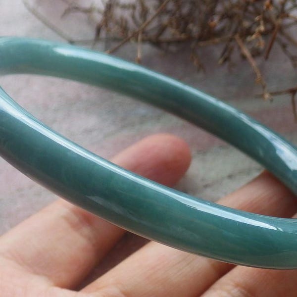 May include: A smooth, polished, circular bangle bracelet in a solid, translucent seafoam green color. The bangle features a rounded, continuous band design with a high-gloss finish that reflects light across its curved, cylindrical surface.