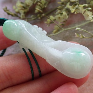 May include: A white jade pendant carved in the shape of a gourd with green accents. The pendant is strung on a green cord.
