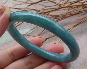 May include: A teal green jade bangle bracelet. The bracelet is smooth and polished.
