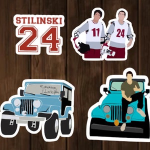 May include: Four stickers featuring characters and a jeep from the TV show Teen Wolf. The first sticker is a red and white jersey with the number 24 and the name "Stilinski" on it. The second sticker shows two men wearing jerseys with the numbers 11 and 24. The third sticker is a blue jeep with the words "Remember, I love you" written on the windshield. The fourth sticker shows a man sitting on the hood of a blue jeep.