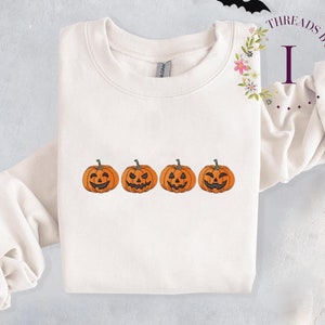Pu&ograve; includere: Felpa bianca con quattro facce di zucca arancione ricamate sul davanti. La felpa ha un collo rotondo e maniche lunghe.