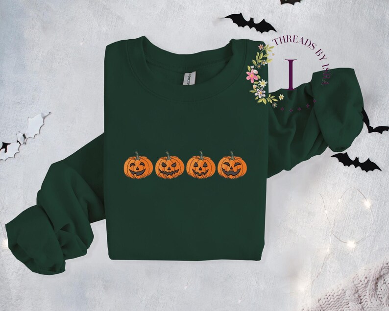 Pu&ograve; includere: Una felpa verde scuro con una fila di quattro zucche arancioni a forma di jack-o'-lantern con facce sorridenti.