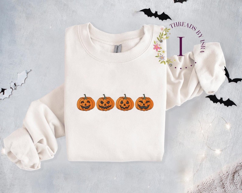 Pu&ograve; includere: Felpa bianca con quattro facce di zucca arancione ricamate sul davanti. La felpa ha un collo rotondo e maniche lunghe.