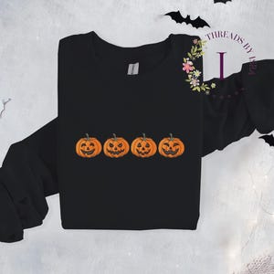 Pu&ograve; includere: Maglietta nera a maniche lunghe con una grafica di quattro zucche arancioni a forma di jack-o'-lantern con diverse espressioni facciali.