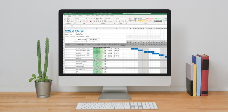 Puede incluir: Un ordenador de sobremesa muestra una hoja de c&aacute;lculo de gesti&oacute;n de proyectos con un diagrama de Gantt. La pantalla muestra un plan de proyecto detallado con duraciones de tareas, dependencias e indicadores de progreso. Tambi&eacute;n se ven un teclado, un cactus en maceta y una pila de libros.