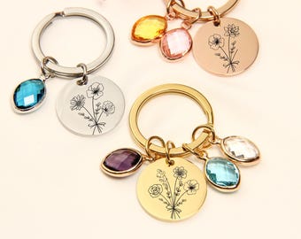 May include: Keychains with floral designs and gemstone accents. The keychains feature round metal pendants engraved with delicate flower illustrations. Each keychain has a different colored gemstone, including blue, purple, and clear stones.