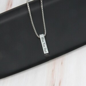 May include: Silver chain necklace with a vertical bar pendant engraved with the words "Miss You Dad".