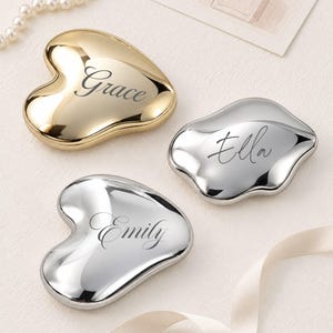 Peut inclure: Trois miroirs de poche en forme de cœur irrégulier avec une finition métallique polie. Un miroir est doré et gravé du prénom Grace, tandis que deux sont argentés et gravés des prénoms Ella et Emily dans une police de caractères cursive.