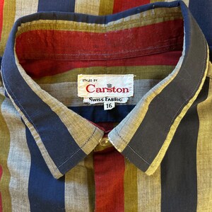 Peut inclure: Une chemise &agrave; boutons ray&eacute;e avec un motif bleu, rouge et vert. La chemise porte une &eacute;tiquette indiquant "Styled by Carston Swiss Fabric 16".